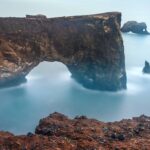 A stunning view of Dyrhólaey, a dramatic coastal arch in South Iceland, with rugged cliffs, black sand beaches, and the vast Atlantic Ocean stretching into the horizon.