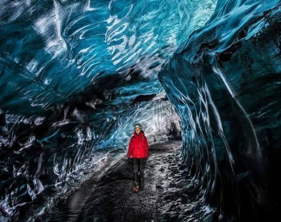 A visitor explores the Crystal Ice Cave, standing still as the light filters through the mesmerizing, icy-blue walls of the glacier.